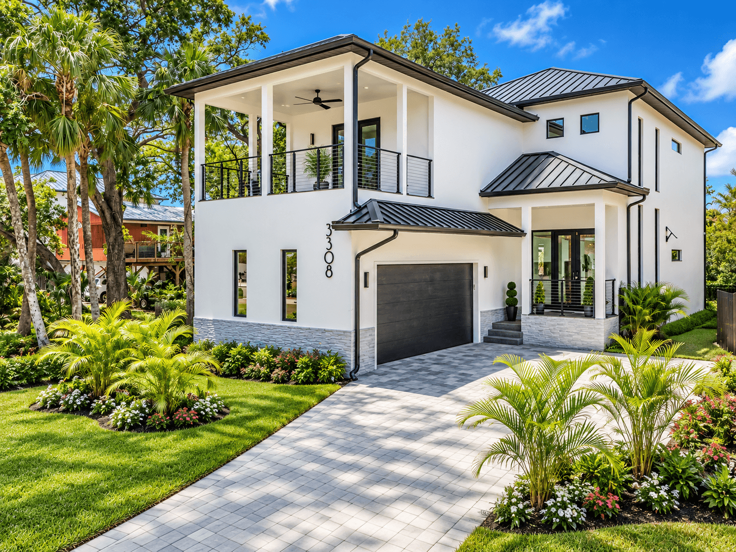 Two-story white residence with a covered balcony, dark garage door and tropical landscaping
